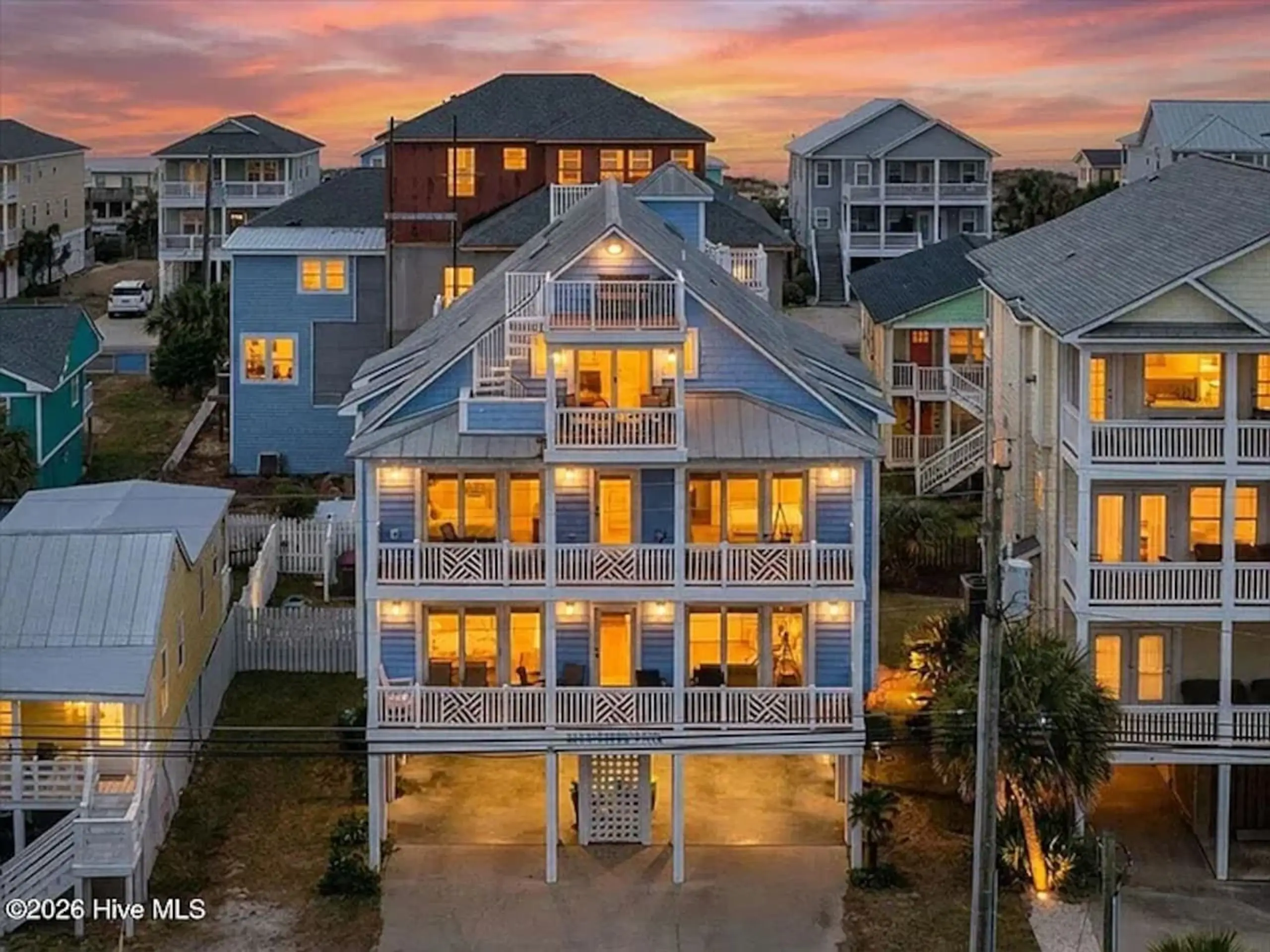 Three-story coastal beach house lit at dusk